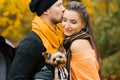 Beautiful couple spend time in a autumn park with their dog friend. A guy kisses a girl
