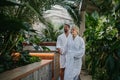 Beautiful couple standing by hot tub, wearing bathrobes, enjoying romantic wellness weekend in spa. Concept of