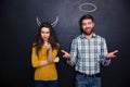 Beautiful couple standing over blackboard with drawn hornes and halo