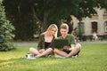 Beautiful couple of students sitting on grass in university campus and using laptop with smile on face. Positive young people