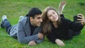 Beautiful couple takes selfie lying on green grass. Media. Young man and woman are photographed on phone lying on grass
