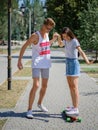 An attractive smiling fellow teaching a girl riding on a longboard in a park on a natural blurred background. Royalty Free Stock Photo