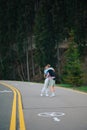 Beautiful couple tourists of young lovers kissing and hugging on a walk in the woods, standing on an asphalt road against the Royalty Free Stock Photo