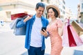 Beautiful couple on vacation smiling happy holding shopping bags using smartphone at street of city Royalty Free Stock Photo