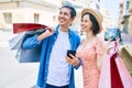 Beautiful couple on vacation smiling happy holding shopping bags using smartphone at street of city Royalty Free Stock Photo