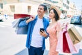 Beautiful couple on vacation smiling happy holding shopping bags using smartphone at street of city Royalty Free Stock Photo