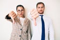 Beautiful couple wearing business clothes looking unhappy and angry showing rejection and negative with thumbs down gesture