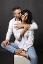 Beautiful couple wearing white shirts and jeans are sitting on a white cube. Man passionately hugs a girl whose shoulder is bare. Royalty Free Stock Photo