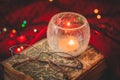 Beautiful cozy christmas winter scene with a book, eyeglasses, a burning candle and glowing xmas garland close-up