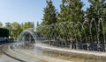 Beautiful Crater Fountain Water in sparkling arc fall on stone. People rest in shade of Evergreen Magnolia Grandiflora Royalty Free Stock Photo