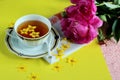 Beautiful cup of tea and floating yellow flowers on a yellow background with a bouquet of red peonies