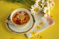 Beautiful cup of tea and floating yellow flowers on a yellow background with a bouquet of red peonies