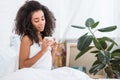 Beautiful curly african american girl holding cup of coffee in bed during morning time Royalty Free Stock Photo