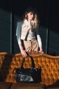 beautiful curly blond hair woman posing with a small black shopper bag near vintage volor sofa