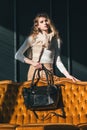 beautiful curly blond hair woman posing with a small black shopper bag near vintage volor sofa