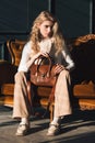 beautiful curly blond hair woman posing with a small brown leather bag on a vintage volor sofa