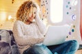 Beautiful curly blonde adult woman use computer laptop in the bedroom at home or hotel - enjoying free office job and freelance