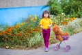 Beautiful curly girl child in a yellow t-shirt and burgundy pants walks with a stroller with a teddy bear near the house. there Royalty Free Stock Photo