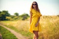 Beautiful curly girl walks on field in summer while wearing a sunglasses and yellow dress. Lifestyle