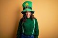 Beautiful curly hair woman wearing green hat with clover celebrating saint patricks day winking looking at the camera with sexy