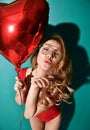 Beautiful curly hair young woman in clear aviator glasses hold big red star balloon blow kiss sign with lips on mint background