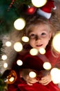 a beautiful curly little girl lies under a Christmas tree with lights in her hair Royalty Free Stock Photo