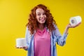 Beautiful curly redhead ginger woman choosing eco toilet paper roll on yellow color background Royalty Free Stock Photo