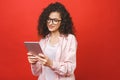 Beautiful curly young girl smiling using and looking at tablet isolated over red background. Copy space Royalty Free Stock Photo