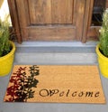 Beautiful cursive welcome peach color doormat with red and black flower plant Placed outside door with green leaves