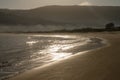 Beautiful curved golden sandy beach with glistening waves in the morning light and fog in the background hills