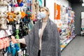 Beautiful customer in mask and scarf on her shoulders carefully examines assortment of pet products indepartment ofhypermarket. Royalty Free Stock Photo