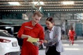 Beautiful customer woman seriously discussing with mechanic man in red uniform about cost of repairing vehicle automobile, auto Royalty Free Stock Photo