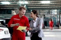 Beautiful customer woman seriously discussing with mechanic man in red uniform about cost of repairing vehicle automobile, auto Royalty Free Stock Photo