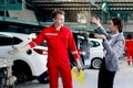 Beautiful customer woman seriously discussing with mechanic man in red uniform about cost of repairing vehicle automobile, auto Royalty Free Stock Photo