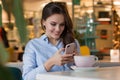 Beautiful cute caucasian young woman in the cafe, using mobile phone and drinking coffee smiling