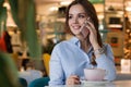 Beautiful cute caucasian young woman in the cafe, using mobile phone and drinking coffee smiling