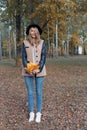 Beautiful cute cheerful girl in a black hat with a bouquet of bright colored leaves in a coat walks in autumn park Royalty Free Stock Photo