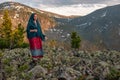 Beautiful cute girl hiker in a dress and a scarf stands on large stones in the mountains