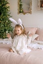 A beautiful cute girl with rabbit ears in a nightgown is sitting on the bed and laughing merrily spreading her arms to the sides. Royalty Free Stock Photo