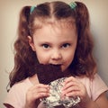 Beautiful cute kid girl eating dark healthy chocolate with fun l