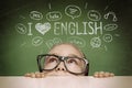 Beautiful cute little girl hiding under table and curiously looking at the illustrations and words in English above her head. Royalty Free Stock Photo