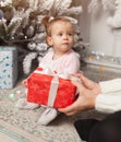 A beautiful cute little girl opens a New Year`s gift. With Christmas tree on the background Royalty Free Stock Photo