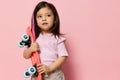 a beautiful cute little girl of preschool age is standing on a pink background in a pink T-shirt and a pink strand in Royalty Free Stock Photo