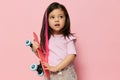 a beautiful cute little girl of preschool age is standing on a pink background in a pink T-shirt and a pink strand in Royalty Free Stock Photo