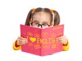 Beautiful cute little girl with glasses reading English grammar book in front of white background. Foreign language learning and s