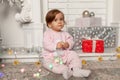 Beautiful cute little girl sitting on the floor near the New Year tree. Holiday mood, childlike spontaneity and sweet atmosphere Royalty Free Stock Photo