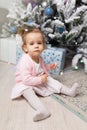 Beautiful cute little girl sitting on the floor near the New Year tree. Holiday mood, childlike spontaneity and sweet atmosphere Royalty Free Stock Photo