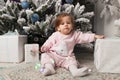 Beautiful cute little girl sitting on the floor near the New Year tree. Holiday mood, childlike spontaneity and sweet atmosphere Royalty Free Stock Photo