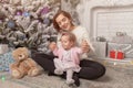 Beautiful cute little girl sitting on the floor near the New Year tree next to her mother. Royalty Free Stock Photo