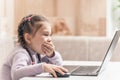 Beautiful cute little girl sitting and laughing cheerfully covering her mouth with her hand, looking at a laptop monitor Royalty Free Stock Photo